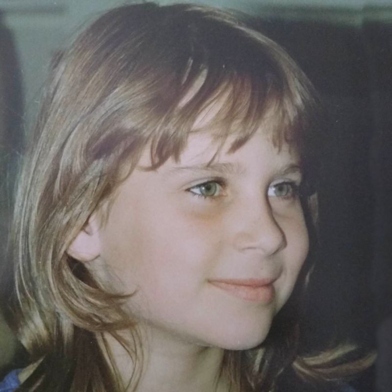 A picture of Julia Harris as a young girl, around nine years old. Julia is turned to the right and smiling. She has dark blond hair, green eyes and pale skin.